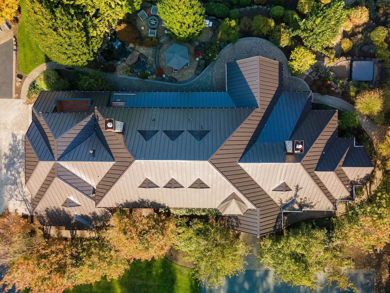 Aerial view of a large residential building with a complex roof design surrounded by trees and landscaping.