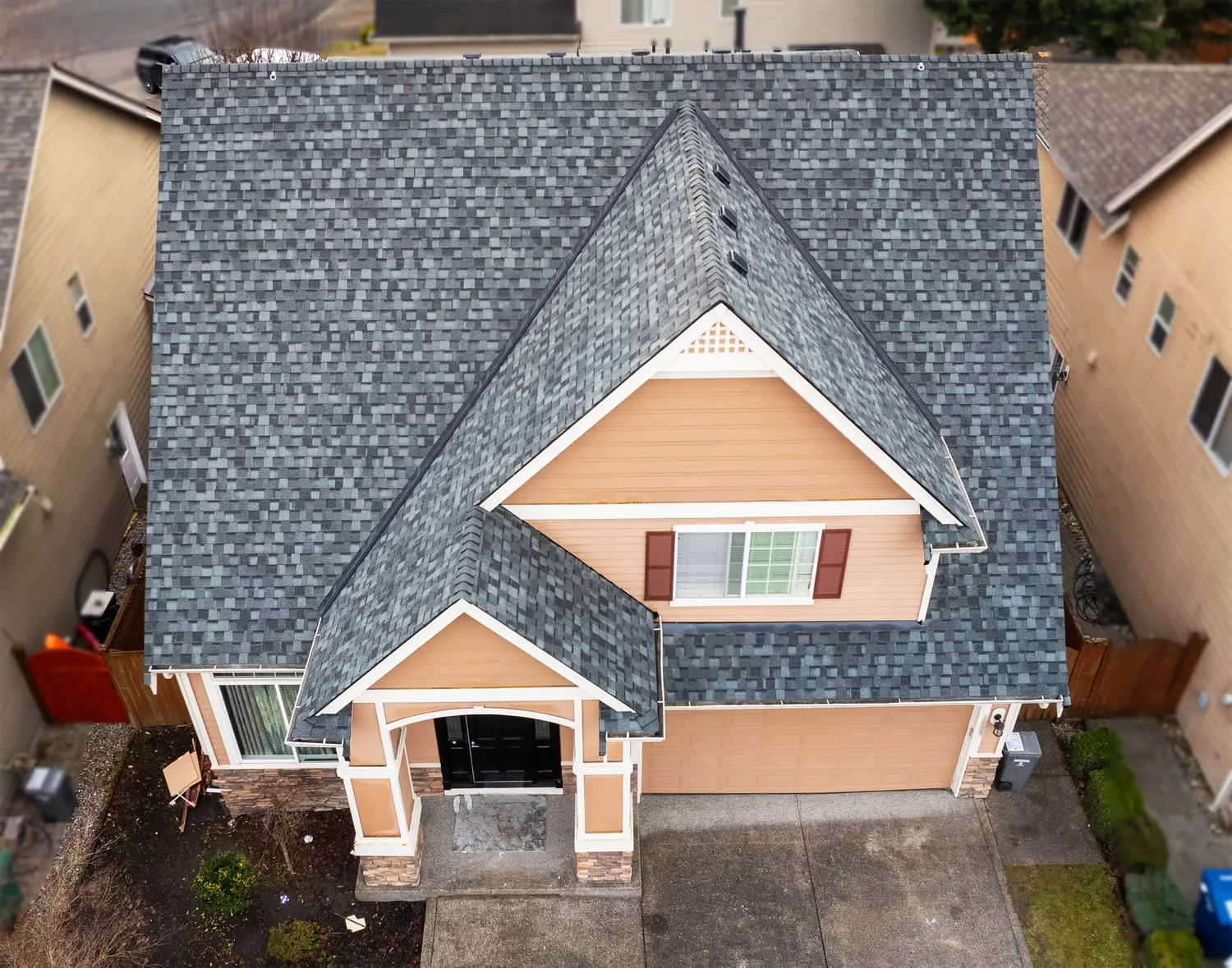 Aerial view of a house with a gray shingle roof and tan siding, surrounded by neighboring homes.