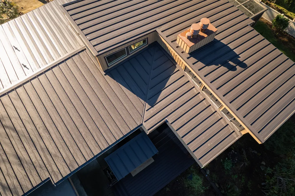 Aerial view of a modern house roof with a metal surface and two chimneys.