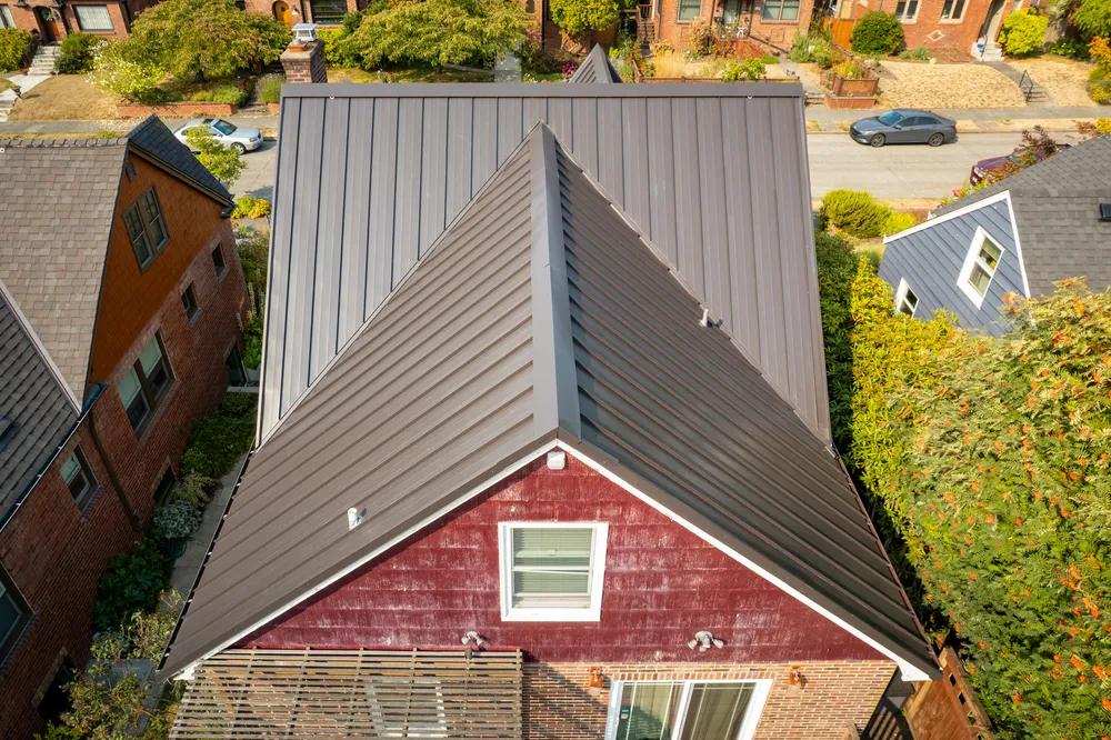 Aerial view of rooftops with a metal roof on a house and a red wooden house adjacent to it.