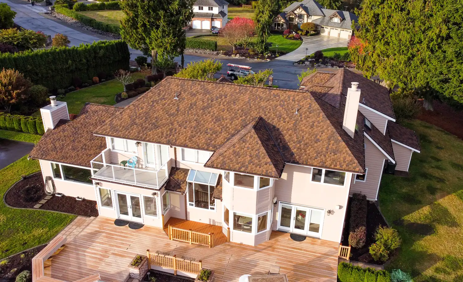 Aerial view of a large house with a brown roof, surrounded by greenery and a driveway leading to the street.