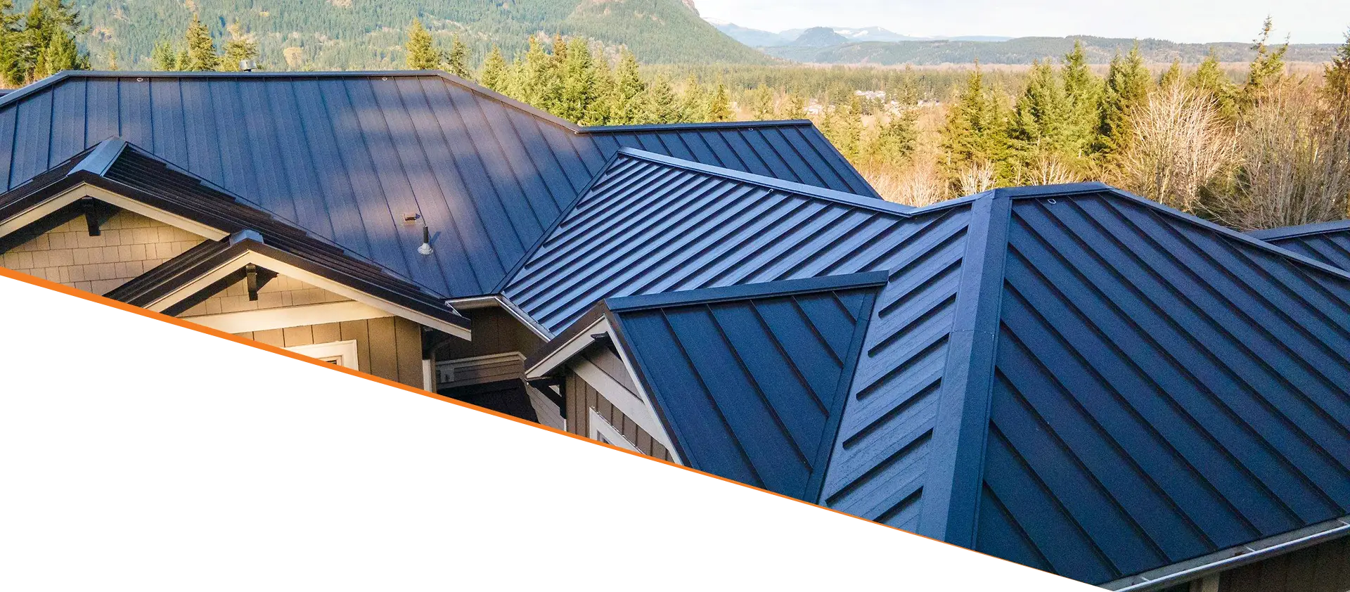 Aerial view of a multi-slope metal roof with a backdrop of green trees and mountains.