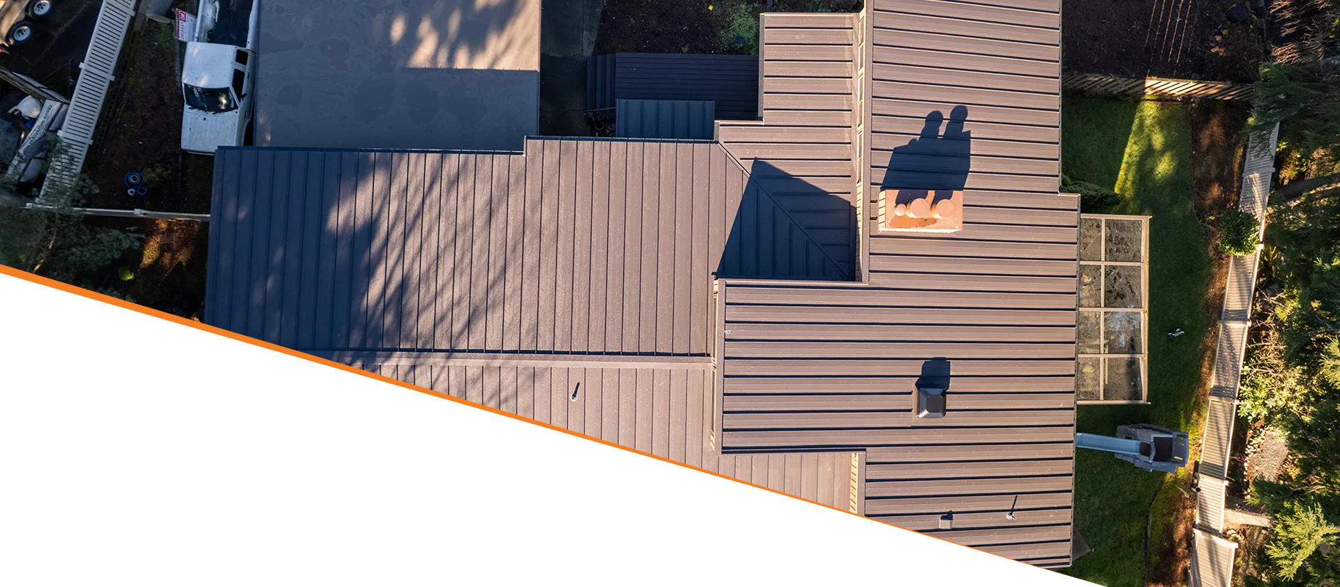 Aerial view of a large home's roof with metal shingles, showcasing varying sections and shadows.