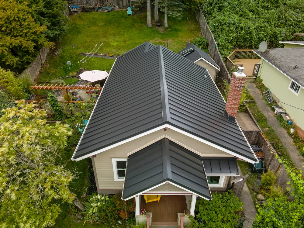 Aerial view of a house with a black metal roof surrounded by greenery and a yard.