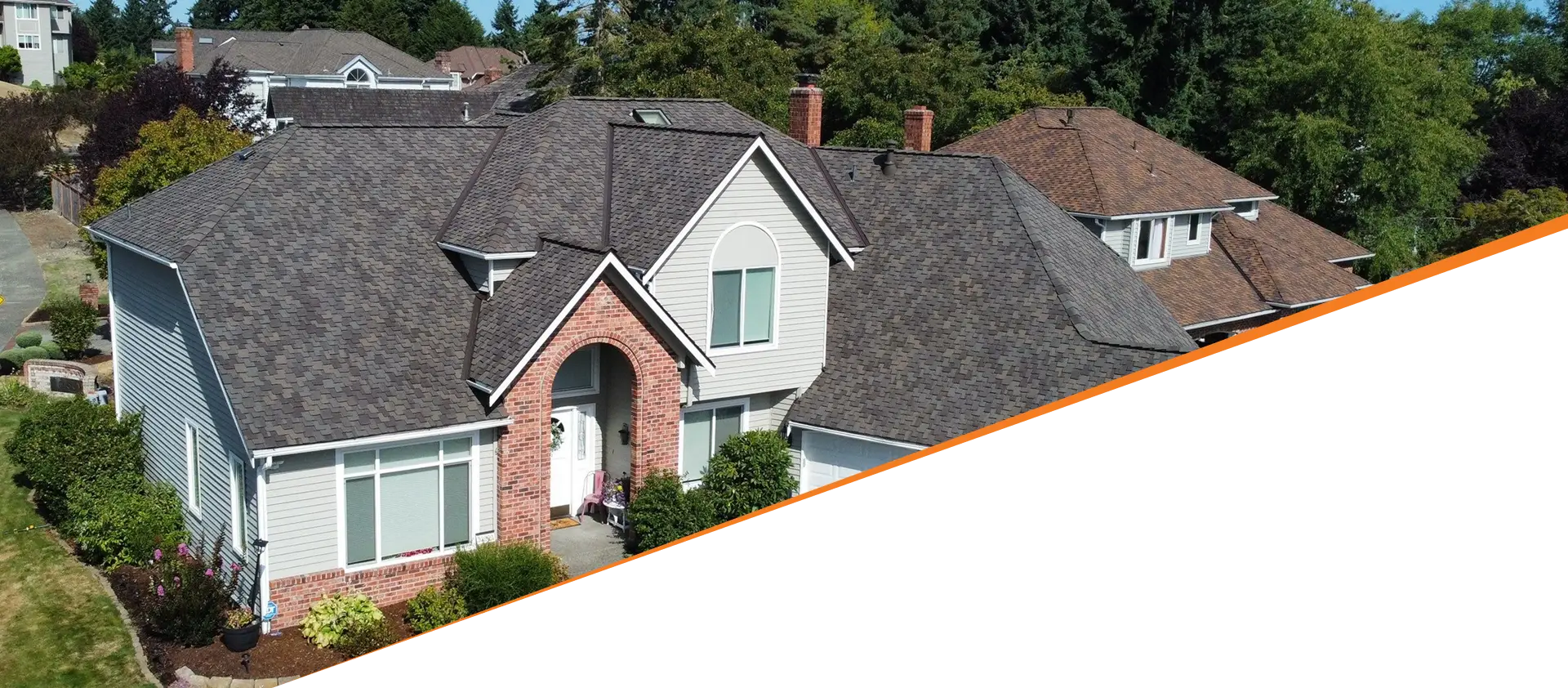 Aerial view of a single-family home with a grey roof, brick accents, and well-maintained landscaping, surrounded by trees and other houses.