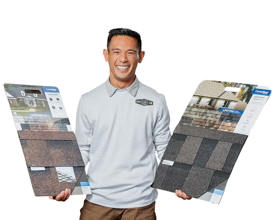 A smiling man holding two display boards of roofing shingles and materials.