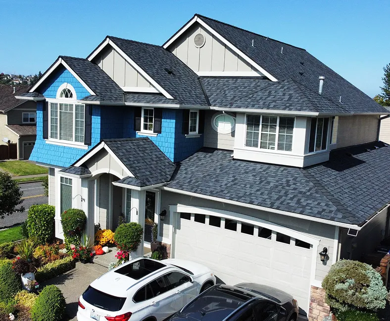 Aerial view of a modern two-story house with a blue and gray exterior, landscaped front yard, and parked cars in the driveway.