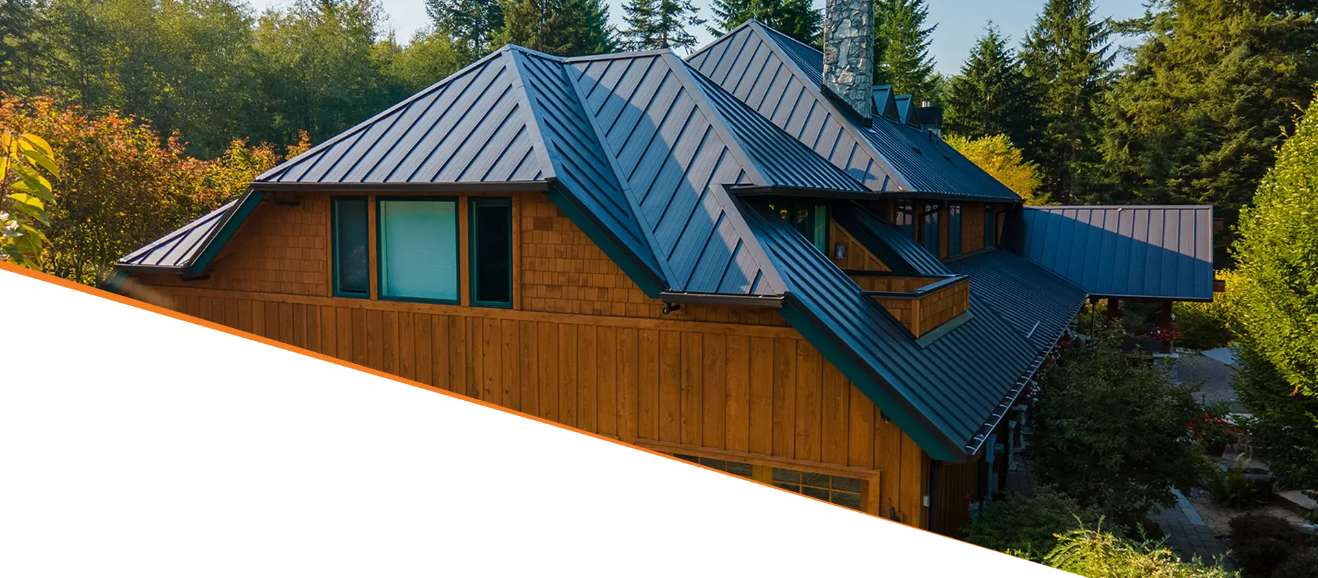 A modern house with a sloped metal roof, featuring a mix of wood and large windows, surrounded by lush greenery.