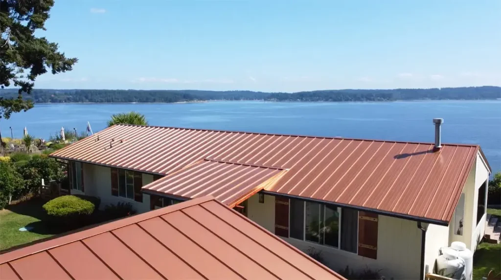 A view of a house with a metal roof, overlooking a body of water and a clear blue sky.