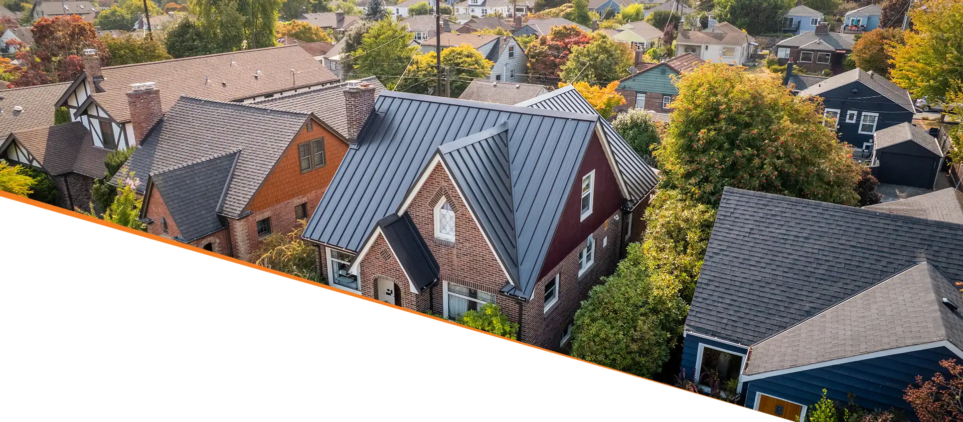 An aerial view of a neighborhood showing various houses with different styles and colors, surrounded by trees and greenery.