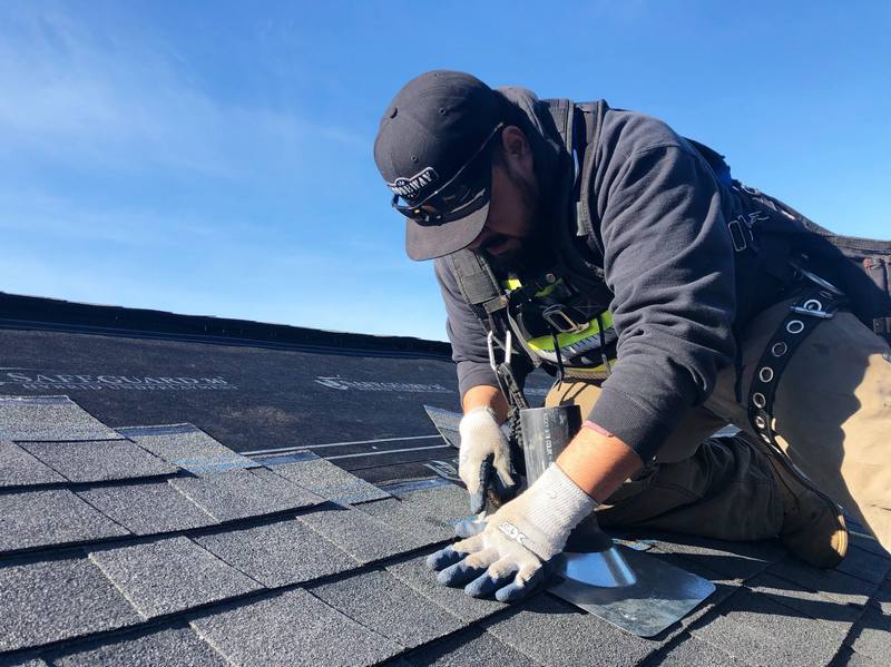 A worker installing shingles on a rooftop on a clear day.