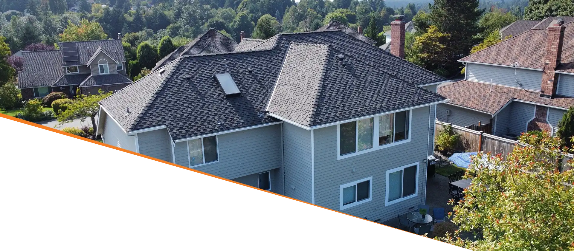 Aerial view of a two-story house with a gray roof and multiple windows, surrounded by trees and other homes.