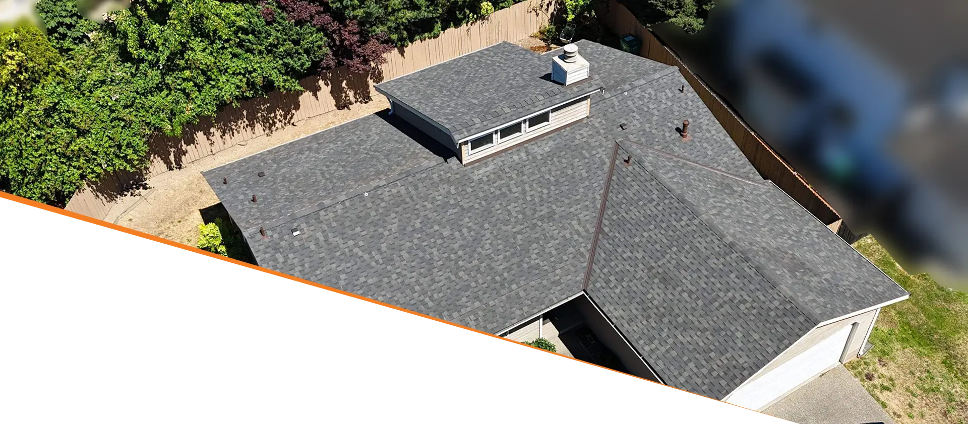 Aerial view of a house with a dark gray roof and a small chimney, surrounded by trees.