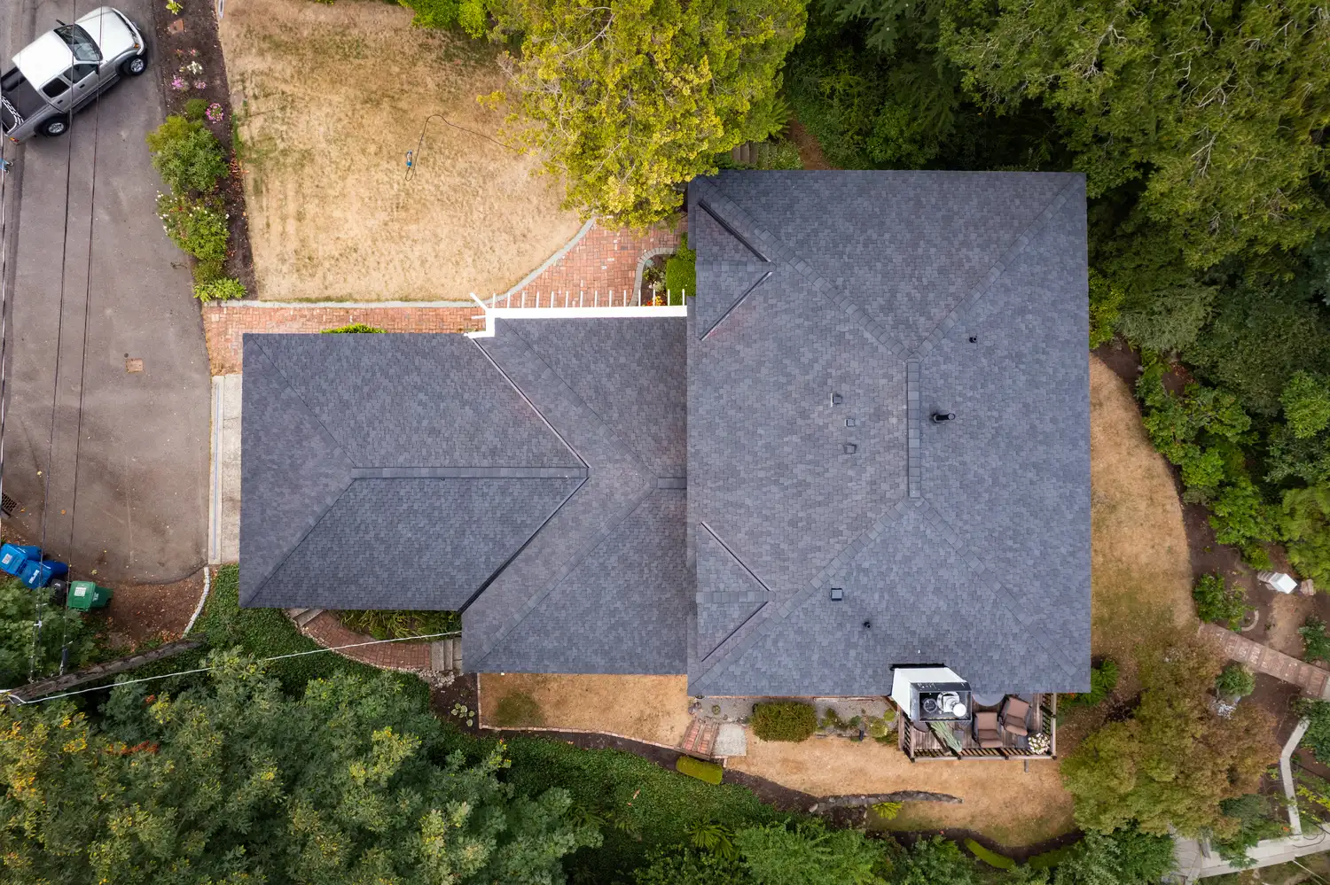 Aerial view of two houses with dark roofs surrounded by trees and a landscaped yard.