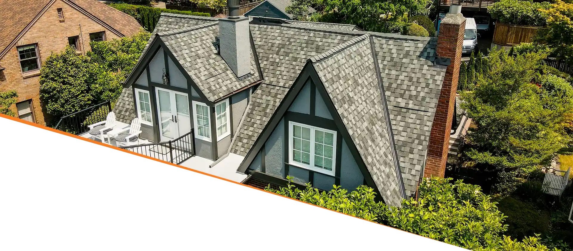 Aerial view of a house with a grey shingled roof and white trim surrounded by greenery.