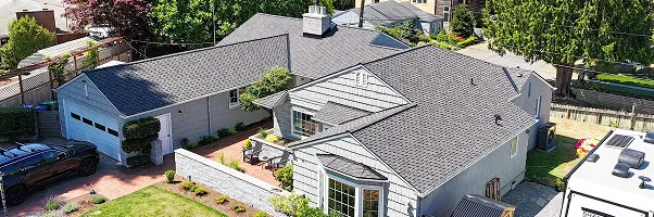 An aerial view of a modern house with a gray exterior, featuring a driveway, garden, and surrounding trees.
