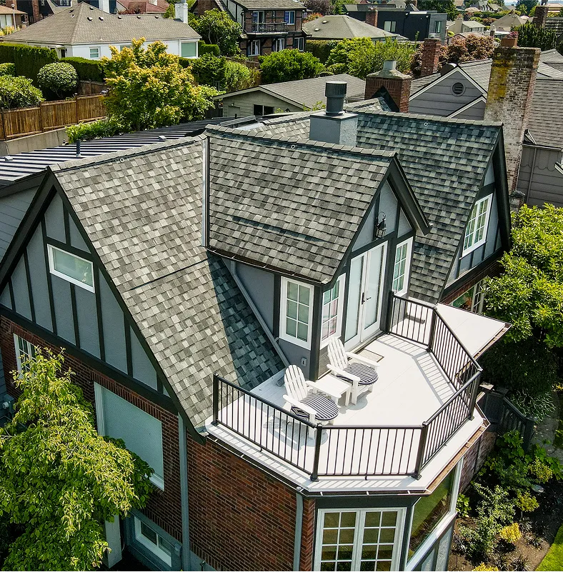 Aerial view of a house with a gray shingle roof, a balcony with two white chairs, and surrounded by greenery.