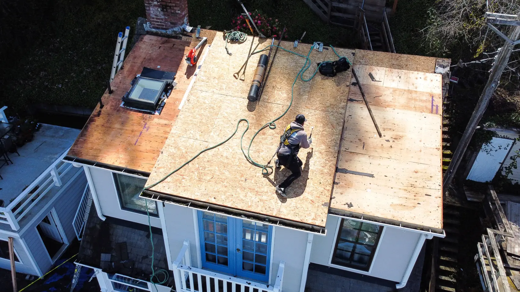 Aerial view of a house under construction with workers on the roof, laying down plywood.