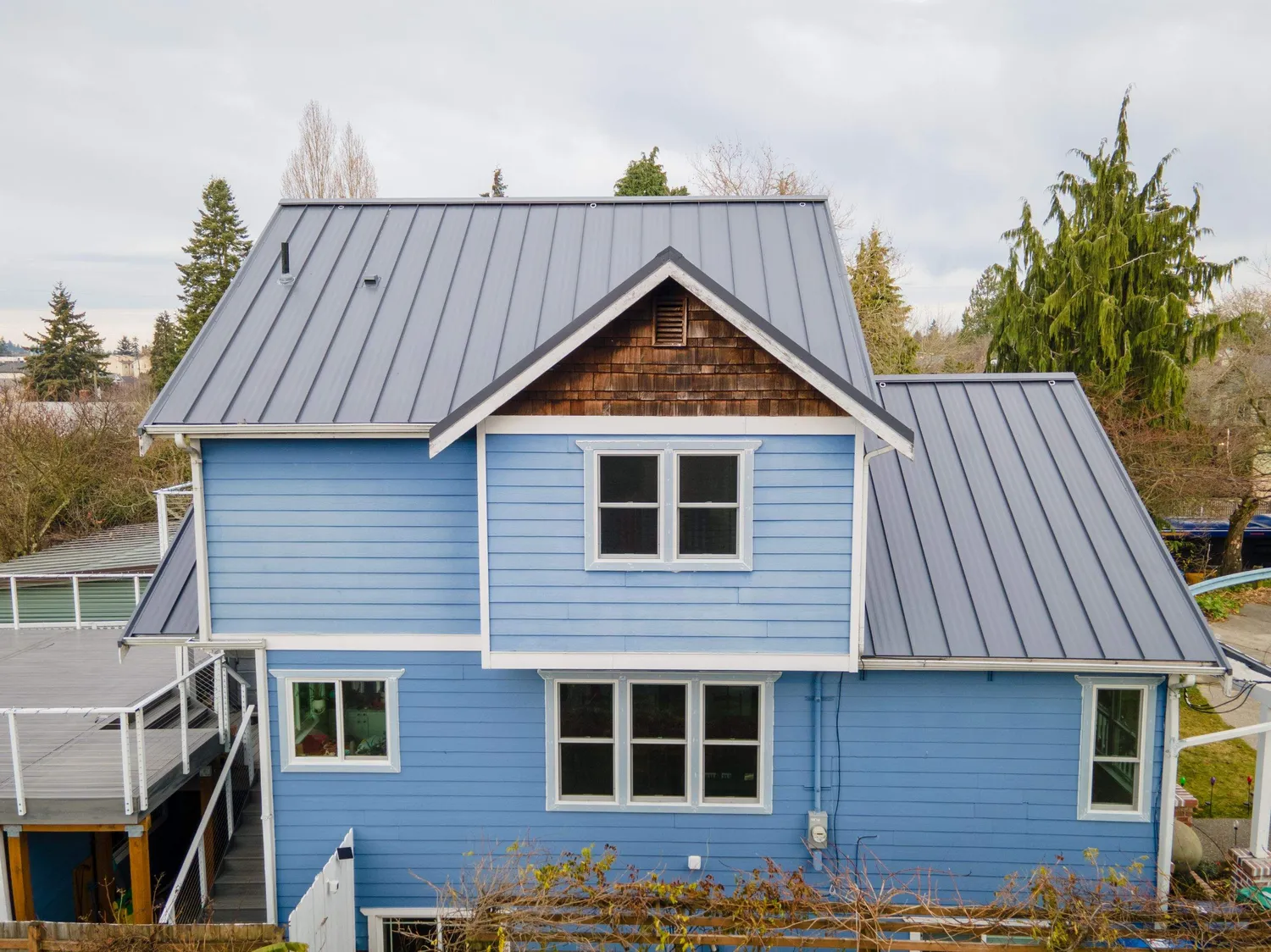 A blue house with a metal roof and wooden shingles, surrounded by trees.