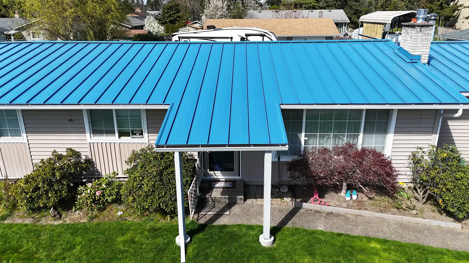 A house with a blue metal roof and a front porch, surrounded by greenery.