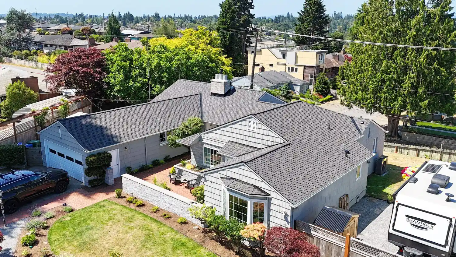 Aerial view of a suburban neighborhood showing several houses with different roof styles and plenty of greenery, including trees and shrubs.