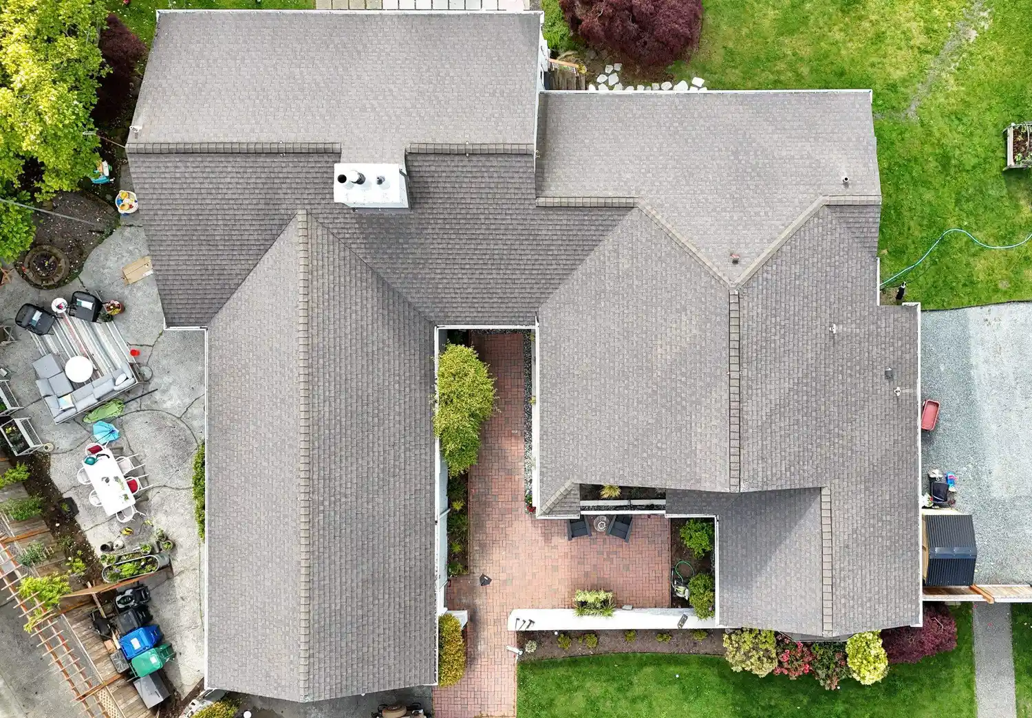 Aerial view of a large house with a complex roof structure, surrounded by green lawn and landscaped gardens.