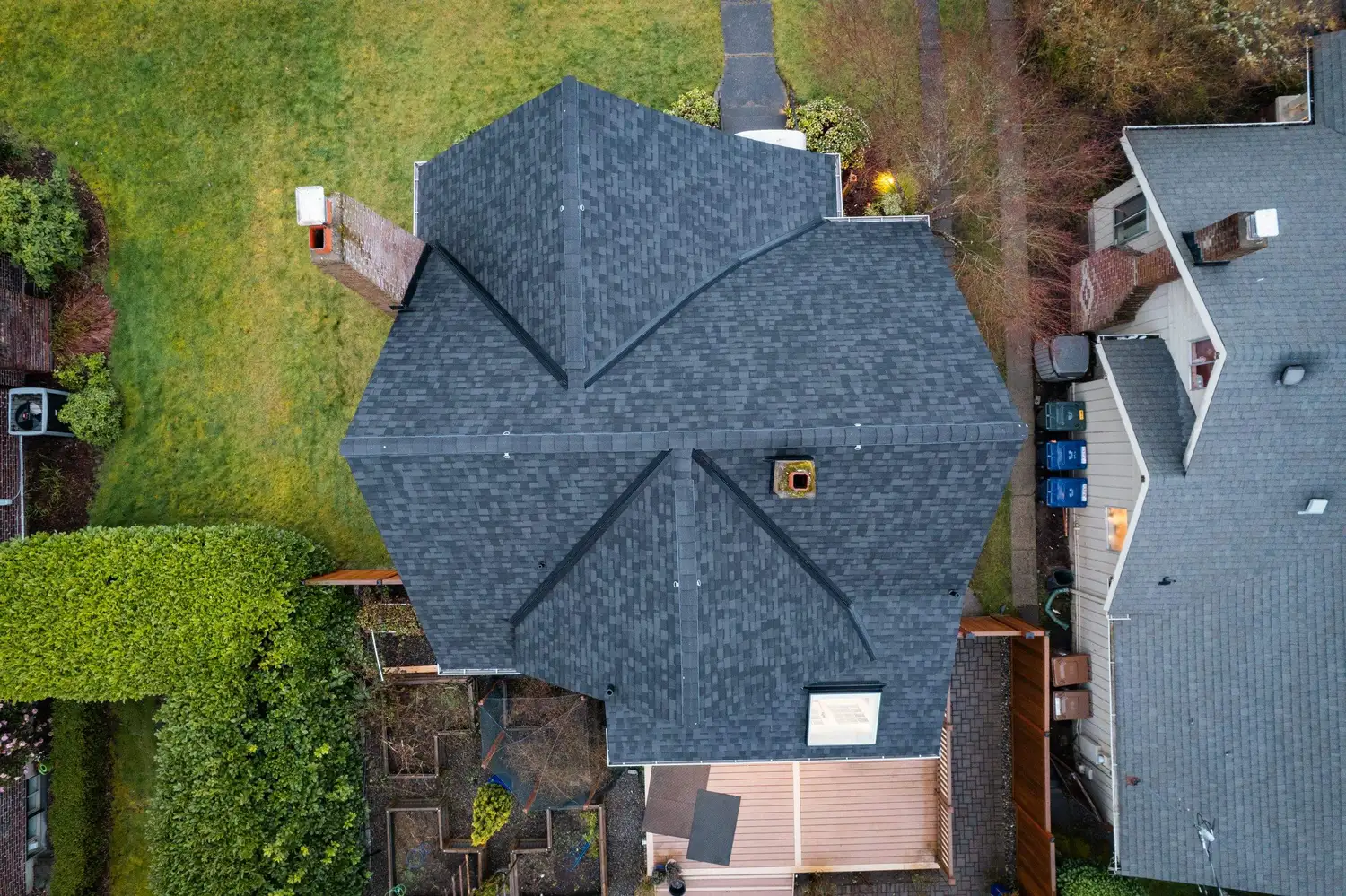 Aerial view of a sloped roof with dark shingles, surrounded by greenery and neighboring houses.