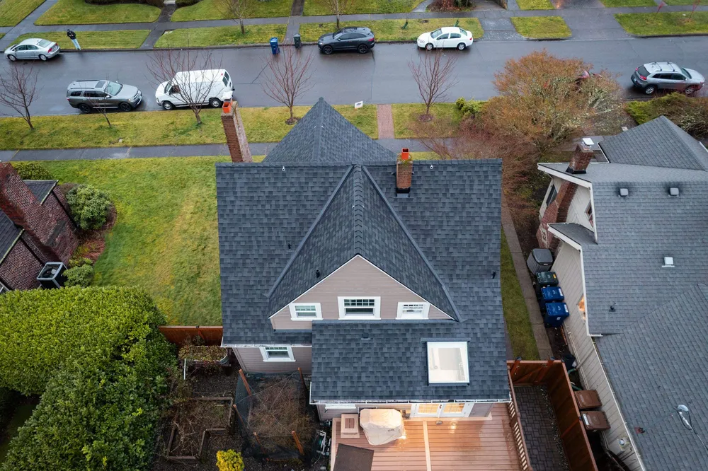 Aerial view of residential houses with green lawns and parked cars on the street.