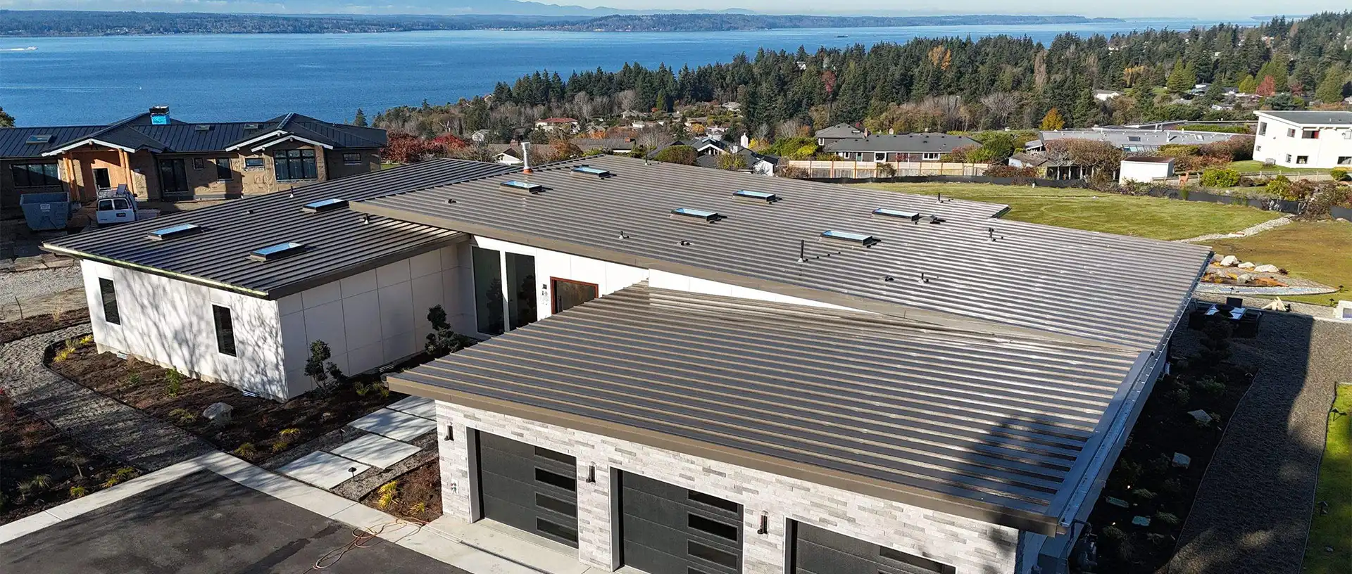 Aerial view of modern homes with metal roofs overlooking a body of water and wooded landscape.