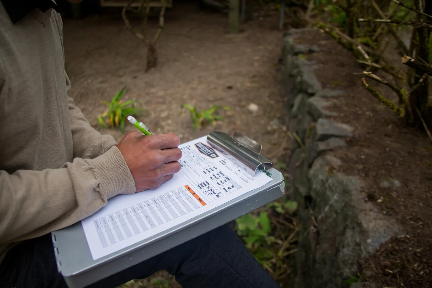 A person writing on a clipboard while sitting outdoors.