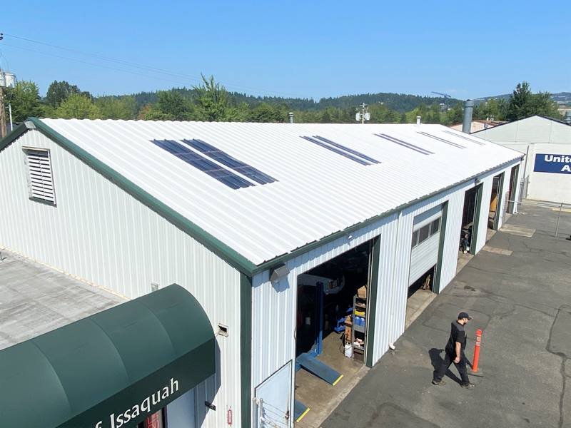 A building with a white metal roof and solar panels, featuring open garage doors and a person walking by.