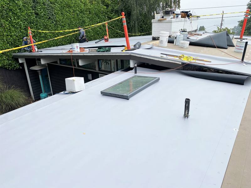 A partially completed roof installation with workers, safety cones, and construction materials.